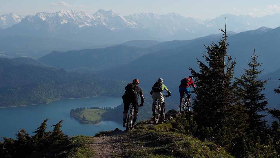 A group of three people biking across a mountain with a lake in the distance.