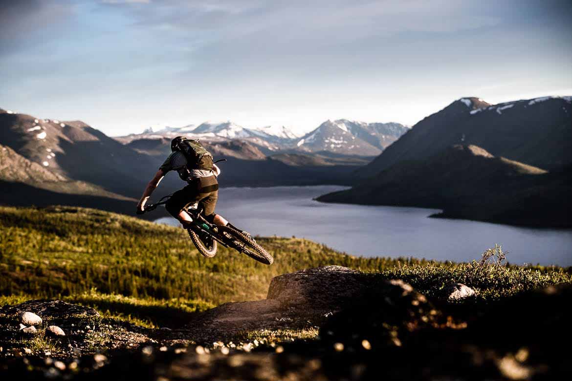 A person biking next to a lake and mountains.